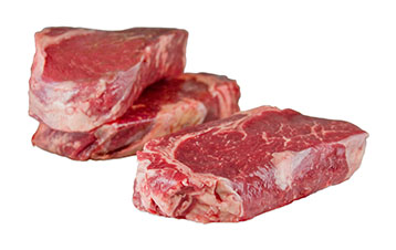 3 raw, grass-fed, ribeye steaks, 1 in the foreground, 2 stacked in the background