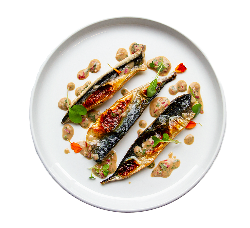 3 whole grilled mackerel on a round white plate with dots of brown sauce, tiny red flowers, and microgreens