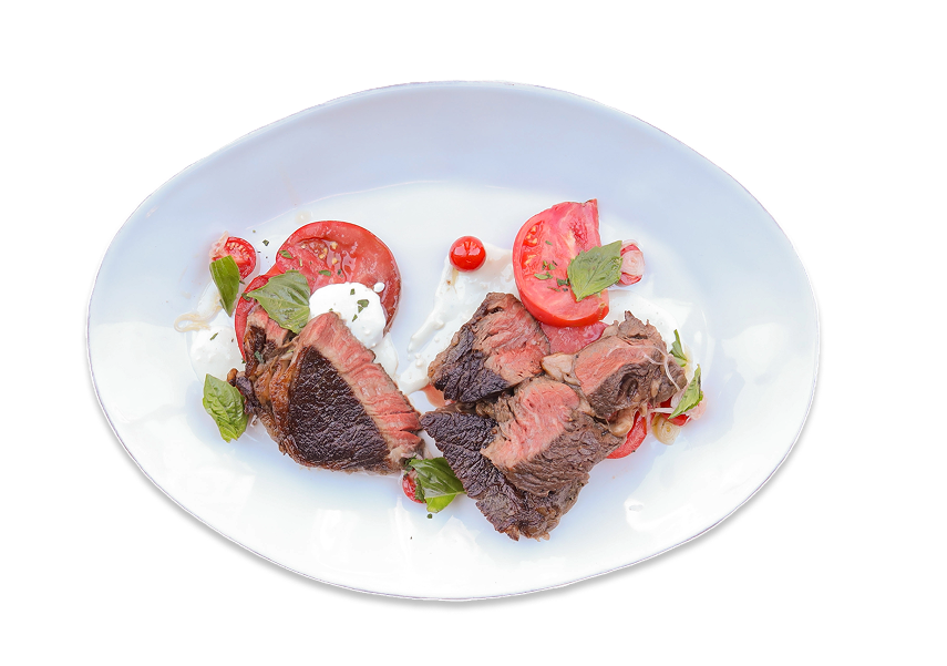 Cooked & sliced Pure Black Wagyu Beef Ribeye on a round, white plate with heirloom tomatoes, basil leaves & a dollop of blue cheese dressing.